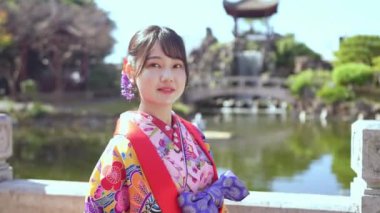Geleneksel Ryusou giyimli, yirmili yaşlarında genç bir kadın Okinawa 'da Çin tarzı bir bahçede kameraya bakıyor ve manzaranın kültürel zarafetini ve manzarasının güzelliğini vurguluyor..