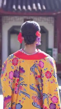 Geleneksel Ryusou giyen yirmili yaşlarında genç bir kadın Okinawa 'da Çin tarzı bir bahçede yürüyor. Bu sahne kültürel miras ve doğal güzelliğin karışımını vurgular..