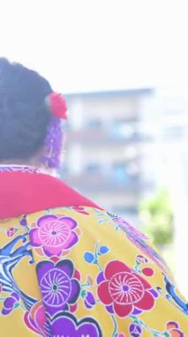 Geleneksel Ryusou giyen yirmili yaşlarda genç bir kadın Okinawa 'da deniz kenarında merdiven kullanıyor. Bu dikey video, kültürel mirasın ve deniz kenarındaki doğal güzelliğin karışımını yakalıyor.