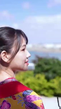 Geleneksel Ryusou giyen yirmili yaşlarında genç bir kadın, elinde plastik bir fincan kahve tutarak Okinawa 'da bir sahil kasabasında yürüyor. Bu dikey video kültürel mirasın karışımını vurguluyor 