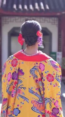 Geleneksel kıyafetler giyen yirmili yaşlarında genç bir kadın Okinawa 'da Çin tarzı bir bahçede yürüyor. Bu dikey yavaş çekim videosu kültürel miras ve doğal güzelliğin karışımını vurguluyor..