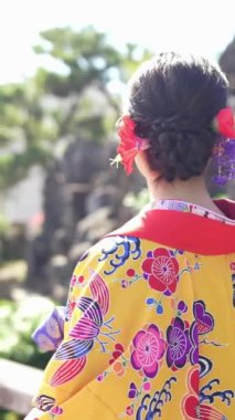 Geleneksel kıyafetler giyen yirmili yaşlarında genç bir kadın Okinawa 'da Çin tarzı bir bahçede yürüyor. Bu dikey yavaş çekim videosu kültürel miras ve doğal güzelliğin karışımını vurguluyor..