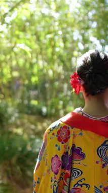 Geleneksel kıyafetler giyen yirmili yaşlarında genç bir kadın Okinawa 'da Çin tarzı bir bahçede yürüyor. Bu dikey yavaş çekim videosu kültürel miras ve doğal güzelliğin karışımını vurguluyor..