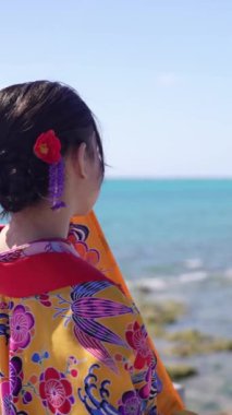 Geleneksel giysiler içinde yirmili yaşlarda genç bir kadın modernlik ve geleneğin karışımını yakalayan nefes kesici bir yavaş çekim videosuyla zarif bir şekilde okyanusun kenarında yürüyor..