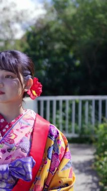Geleneksel kıyafetler giyen yirmili yaşlarında genç bir kadın Okinawa 'da bir kasabada yürüyor. Bu dikey yavaş çekim videosu kültürel miras ve kentsel yaşamın karışımını vurguluyor.