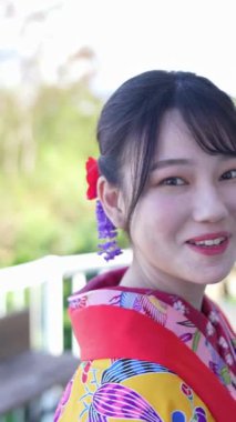 Geleneksel kıyafetler giyen yirmili yaşlarında genç bir kadın Okinawa 'da bir kasabada yürüyor. Bu dikey yavaş çekim videosu kültürel miras ve kentsel yaşamın karışımını vurguluyor.