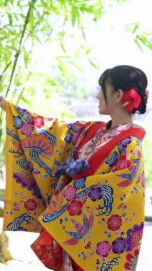 20 'li yaşlarda, geleneksel kıyafetler giyen genç bir kadın Okinawa' da Çin tarzı bir bahçede akıllı telefonuyla selfie çekiyor. Bu dikey yavaş çekim videosu karışımı vurgular