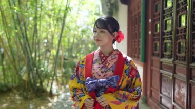 Yavaş çekimde, geleneksel Okinawa giysisine benzeyen bir kimono giymiş genç bir Japon kadın Çin tarzı bir bahçe içinde zarif bir bambu koruluğunun içinden geçerek huzurlu ve büyüleyici bir sahne yaratıyor..