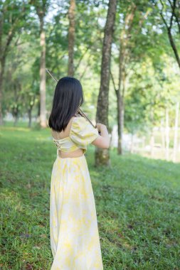 Serin bir fotoğraf, 20 'li yaşlarda, çarpıcı sarı bir elbise giymiş, Kuala Lumpur' da bereketli, doğa dolu bir parkta zarif bir şekilde keman çalan genç bir Çinli-Malezyalı kadını resmediyor.