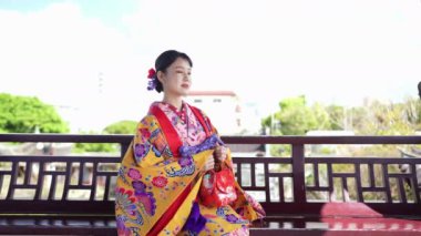 Geleneksel kıyafet giymiş 20 'li yaşlarda Japon bir kadın deniz kenarında akıllı telefonunu kullanıyor. Bu dikey yavaş çekim videosu, modern teknolojinin kültürel miras ile karışımını vurguluyor..