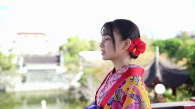 Okinawa 'nın zarif Ryuso' suyla süslenmiş genç bir Japon kadının Çin 'den esinlenilmiş bir bahçenin yemyeşil yaprakları ve süslü yapıları arasında durduğu ruhsal ağır çekim sahnesi gözler önüne seriliyor., 