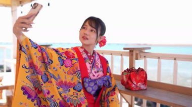 Genç Japon kadın, akışkan Ryuso 'yla süslenirken, görsel terasta kendi portresini ustalıkla yakalar, panoramik okyanus manzaralı, büyüleyici, yavaş çekim..