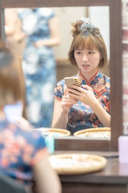 Tayvanlı 20 'li yaşlarda mavi Cheongsam giyen genç bir kadın Wanhua, Taipei, Taiwa' da bir kiralık dükkanda saçını yaptırıyor.