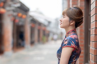 23 'lerinde Tayvanlı genç bir kadın mavi bir keongsam giyiyor, Wanhua, Taipei, Tayvan' ın kültürel bir bölgesinde duruyor ve etrafı gözetliyor.