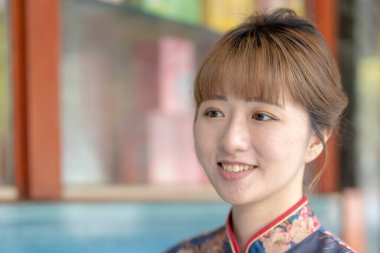 20 'li yaşlardaki Tayvanlı genç bir kadın mavi bir keongsam giyiyor ve kırmızı bir çanta taşıyor. Wanhua Bölgesi, Tayvan sokaklarında geziniyor.