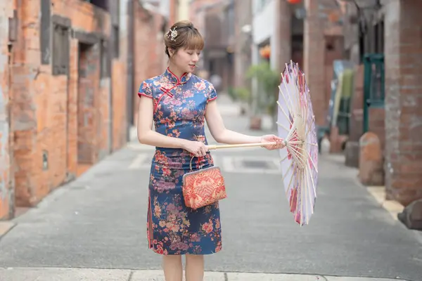 stock image Young Taiwanese woman in her 20s wearing a blue cheongsam, strolling through a cultural district in Wanhua, Taipei, Taiwan, while holding a Chinese-patterned umbrella