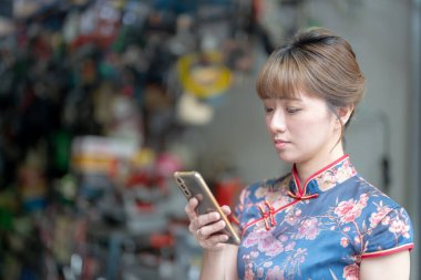 20 'li yaşlardaki Tayvanlı genç bir kadın mavi bir keongsam giyiyor ve kırmızı bir çanta taşıyor. Wanhua Bölgesi, Tayvan sokaklarında geziniyor.