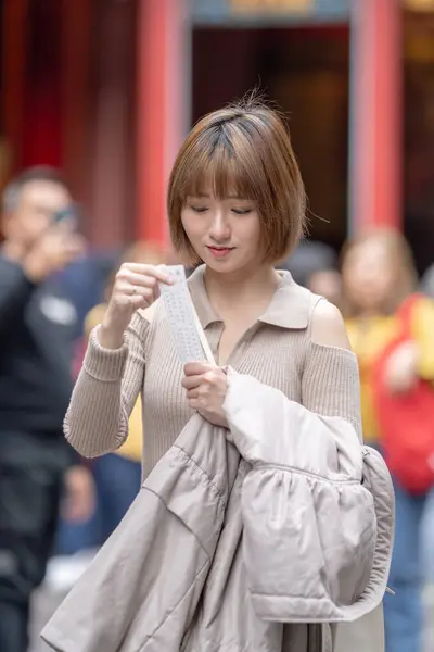 stock image Young Taiwanese woman in her 20s wearing cream-colored clothes, drawing a fortune slip (omikuji) at the famous tourist attraction Longshan Temple in Wanhua District, Taipei, Taiwan