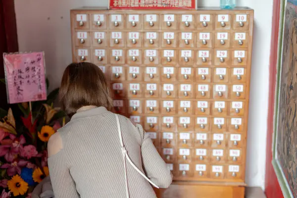 stock image Young Taiwanese woman in her 20s wearing cream-colored clothes, drawing a fortune slip (omikuji) at the famous tourist attraction Longshan Temple in Wanhua District, Taipei, Taiwan