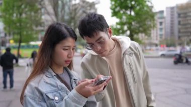 Tayvanlı genç bir kadın yirmili yaşlarında Xinyi İlçesi sokaklarında akıllı telefon kullanıyor ilkbaharda öğlen vakti, yanında kapüşonlu bir adamla. Kadın kot ceket giyiyor..