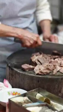 Taipei 'nin Wanhua semtindeki bir alışveriş caddesinde yerel bir restoranın mutfağında hızla et doğrayan Tayvanlı bir kadının dikey videosu..