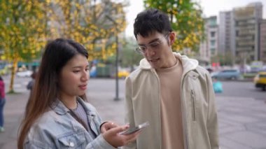 Tayvanlı genç bir kadın yirmili yaşlarında Xinyi İlçesi sokaklarında akıllı telefon kullanıyor ilkbaharda öğlen vakti, yanında kapüşonlu bir adamla. Kadın kot ceket giyiyor..