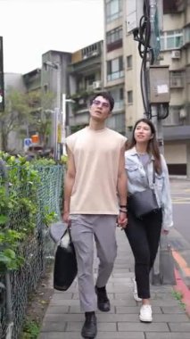 Tayvanlı genç bir çiftin yirmili yaşlarda Taipei 'nin Xinyi İlçesi sokaklarında yürürken çekilmiş dikey bir videosu. Adam kolsuz bir bluz giyiyor ve kadın kot ceket giyiyor..