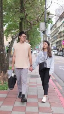 Tayvanlı genç bir çiftin yirmili yaşlarda Taipei 'nin Xinyi İlçesi sokaklarında yürürken çekilmiş dikey bir videosu. Adam kolsuz bir bluz giyiyor ve kadın kot ceket giyiyor..