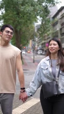 Tayvanlı genç bir çiftin yirmili yaşlarda Taipei 'nin Xinyi İlçesi sokaklarında yürürken çekilmiş dikey bir videosu. Adam kolsuz bir bluz giyiyor ve kadın kot ceket giyiyor..