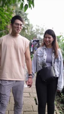 Taipei 'nin Xinyi İlçesi' nde küçük bir patika boyunca yürüyen ve konuşan 20 'li yaşlarda genç bir Tayvanlı çiftin dikey yavaş çekim videosu. Adam kolsuz bir bluz giyiyor.