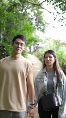 Taipei 'nin Xinyi İlçesi' nde küçük bir patika boyunca yürüyen ve konuşan 20 'li yaşlarda genç bir Tayvanlı çiftin dikey yavaş çekim videosu. Adam kolsuz bir bluz giyiyor.