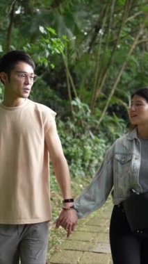 Taipei 'nin Xinyi İlçesi' nde küçük bir patika boyunca yürüyen ve konuşan 20 'li yaşlarda genç bir Tayvanlı çiftin dikey yavaş çekim videosu. Adam kolsuz bir bluz giyiyor.