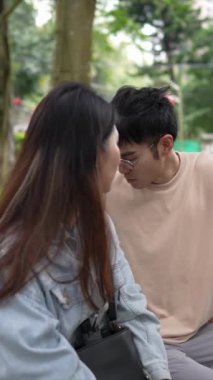 Tayvanlı genç bir çiftin yirmili yaşlarda bir bankta oturup Taipei 'nin Xinyi İlçesi' ndeki bir parkta konuştuğu dikey ağır çekim bir video..