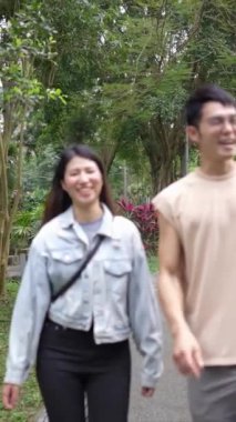 Taipei 'nin Xinyi İlçesi' ndeki bir parkta yirmili yaşlarda genç bir Tayvanlı çiftin bahar öğleden sonra yürüdüğü dikey ağır çekim bir video. Adam kolsuz bir bluz giyiyor.,