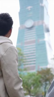 Taipei 'nin Xinyi İlçesi, Taipei İlçesi' nde, arka planda Taipei 101 ile yirmili yaşlarda genç bir Tayvanlı çiftin dikey yavaş çekim videosu var..