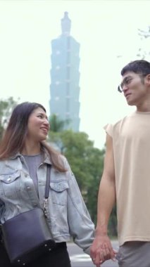 Taipei 'nin Xinyi İlçesi, Taipei İlçesi' nde, arka planda Taipei 101 ile yirmili yaşlarda genç bir Tayvanlı çiftin dikey yavaş çekim videosu var..
