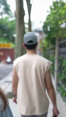 Taipei 'nin Xinyi İlçesi sokaklarında yirmili yaşlarda genç bir Tayvanlı çiftin bahar öğleden sonra yürüdüğü dikey ağır çekim bir video. Adam kolsuz bir bluz giyiyor.