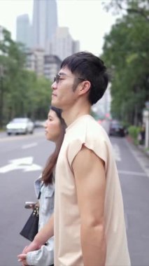 Taipei 'nin Xinyi İlçesi sokaklarında yirmili yaşlarda genç bir Tayvanlı çiftin bahar öğleden sonra yürüdüğü dikey ağır çekim bir video. Adam kolsuz bir bluz giyiyor.
