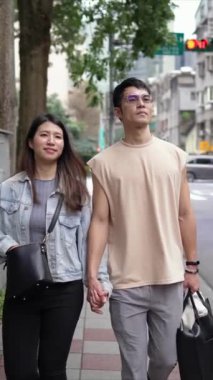 Taipei 'nin Xinyi İlçesi sokaklarında yirmili yaşlarda genç bir Tayvanlı çiftin bahar öğleden sonra yürüdüğü dikey ağır çekim bir video. Adam kolsuz bir bluz giyiyor.