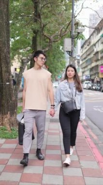 Taipei 'nin Xinyi İlçesi sokaklarında yirmili yaşlarda genç bir Tayvanlı çiftin bahar öğleden sonra yürüdüğü dikey ağır çekim bir video. Adam kolsuz bir bluz giyiyor.