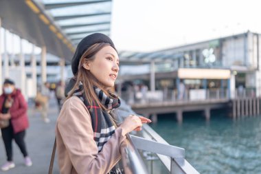 Tsim Sha Tsui, yirmili yaşlarda, kahverengi saçlı, siyah ekose elbiseli, bereli ve mini etekli, Hong Kong 'daki West Kowloon limanının deniz kenarındaki çitlerine yaslanmış bir kadın.