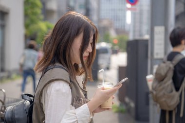 Yazın başlarında, genç bir Çinli değişim öğrencisi, 20 'li yaşlarda, Tokyo, Minato' daki Hamamatsucho İstasyonu 'nun önünde elinde plastik bir bardakta buzlu bir au lait tutuyor..