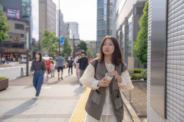 Yazın başlarında, genç bir Çinli değişim öğrencisi, 20 'li yaşlarda, Tokyo, Minato' daki Hamamatsucho İstasyonu 'nun önünde elinde plastik bir bardakta buzlu bir au lait tutuyor..