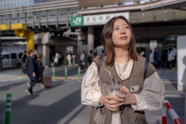 Yazın başlarında, genç bir Çinli değişim öğrencisi, 20 'li yaşlarda, Tokyo, Minato' daki Hamamatsucho İstasyonu 'nun önünde elinde plastik bir bardakta buzlu bir au lait tutuyor..
