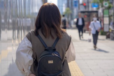 Yazın başlarında, genç bir Çinli değişim öğrencisi, 20 'li yaşlarda, Tokyo, Minato' daki Hamamatsucho İstasyonu 'nun önünde elinde plastik bir bardakta buzlu bir au lait tutuyor..