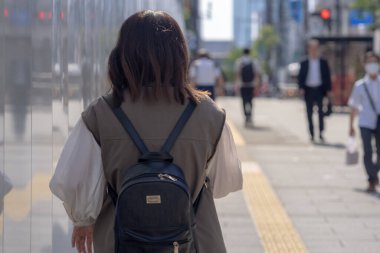Yazın başlarında, genç bir Çinli değişim öğrencisi, 20 'li yaşlarda, Tokyo, Minato' daki Hamamatsucho İstasyonu 'nun önünde elinde plastik bir bardakta buzlu bir au lait tutuyor..