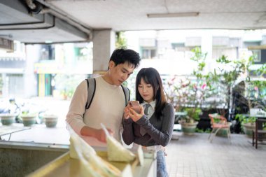 Mart, Zhongshan Anıt Salonu yakınlarındaki Zhongzheng İlçesi, Taipei Şehri, Tayvan, yirmili yaşlarda Tayvanlı bir kadın ve Hong Kong 'lu bir adam yerel dükkanda soya sütü ve turp keki yiyorlar..