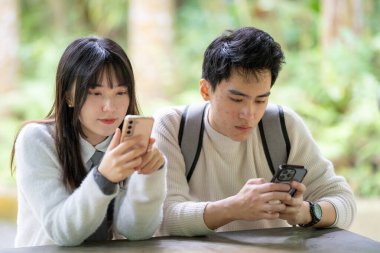 Mart ayında, Tayvanlı bir kadın ve Hong Kong 'lu bir adam Zhongzheng Bölgesi, Taipei City, Tayvan' da yemyeşil bir botanik bahçesinde, akıllı telefon kullanarak ve sohbet ederek mutlu mesut oturuyorlar..