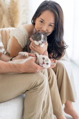 Selangor, Malezya 'da, uzun saçlı Çinli Malezyalı kadın ve Hint kökenli erkek çift Asya' dan esinlenilmiş mobilyalarla şık bir odada, siyah beyaz kediyle oynuyorlar..