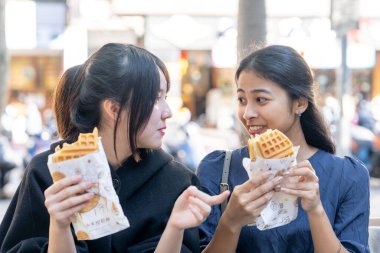 Tayvanlı bir kadın, Tayvanlı bir erkek ve Asyalı bir kadın, Taipei 'de Daan Bölgesi' nde bir bankta oturmuş, büyük bir waffle 'ın keyfini çıkarıyorlar..